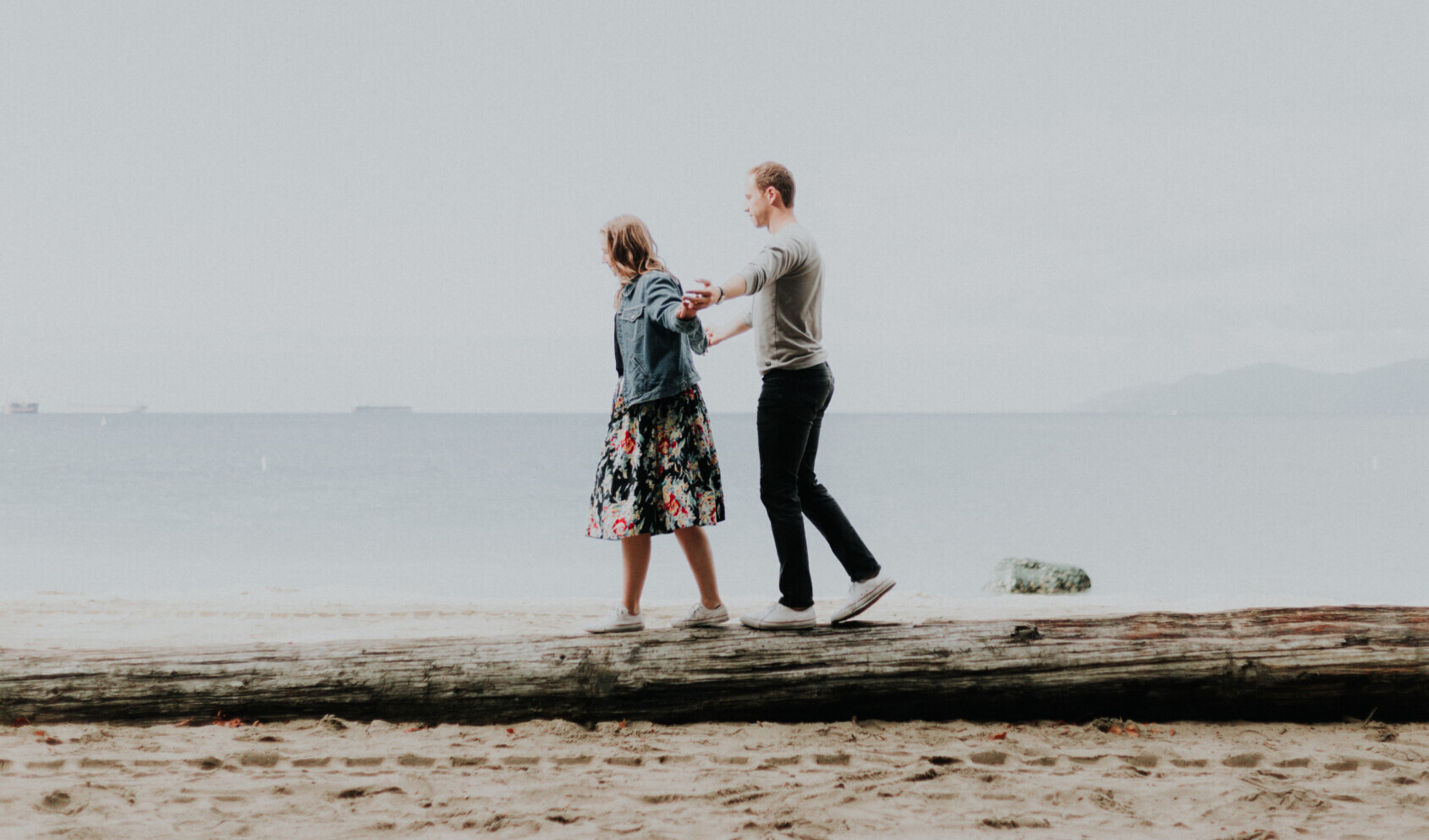 Couple walking together on a driftwood log at the beach